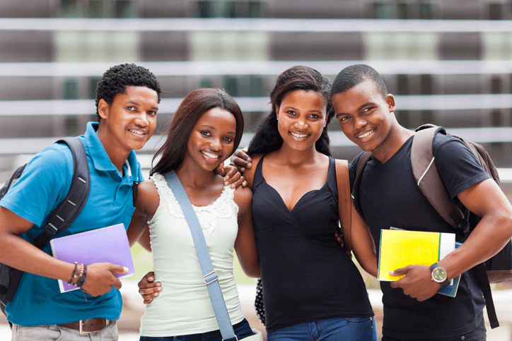 Quatro estudantes sorridentes com cadernos e mochilas